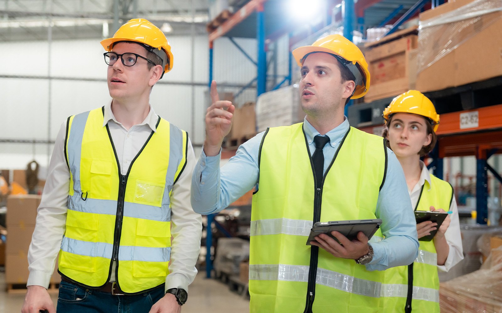 Team mit Helmen und Tablets in Lagerhalle – Symbolbild für Vorbereitung der Unterweisung im Arbeitsschutz